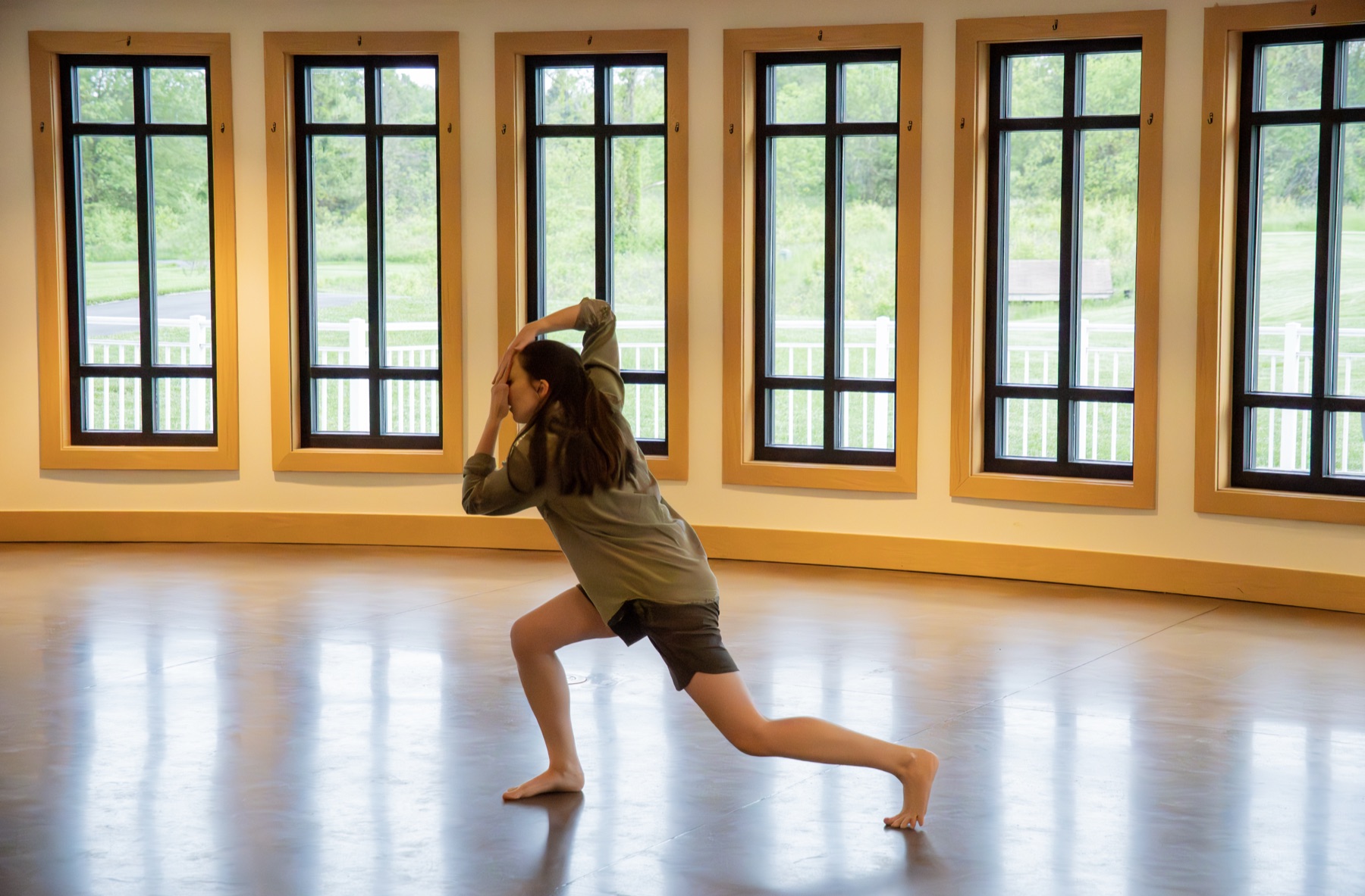 A dancer in a deep lunge in a bright studio lined with windows