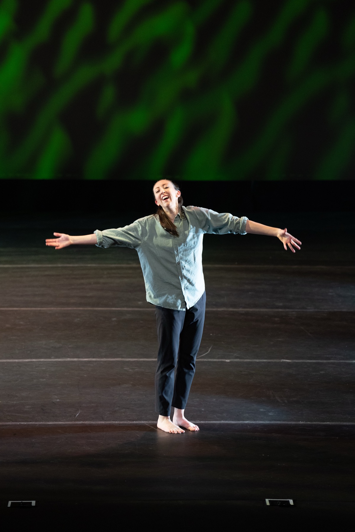 Ashlyn Hall performing on stage with arms outstretched in front of a green projection